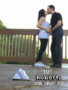 A picture showing a pair of baby-sized shoes resting in the foreground, as me and my husand kiss in the background. It is accomapnied by the words: Baby Roberts, coming 2018.